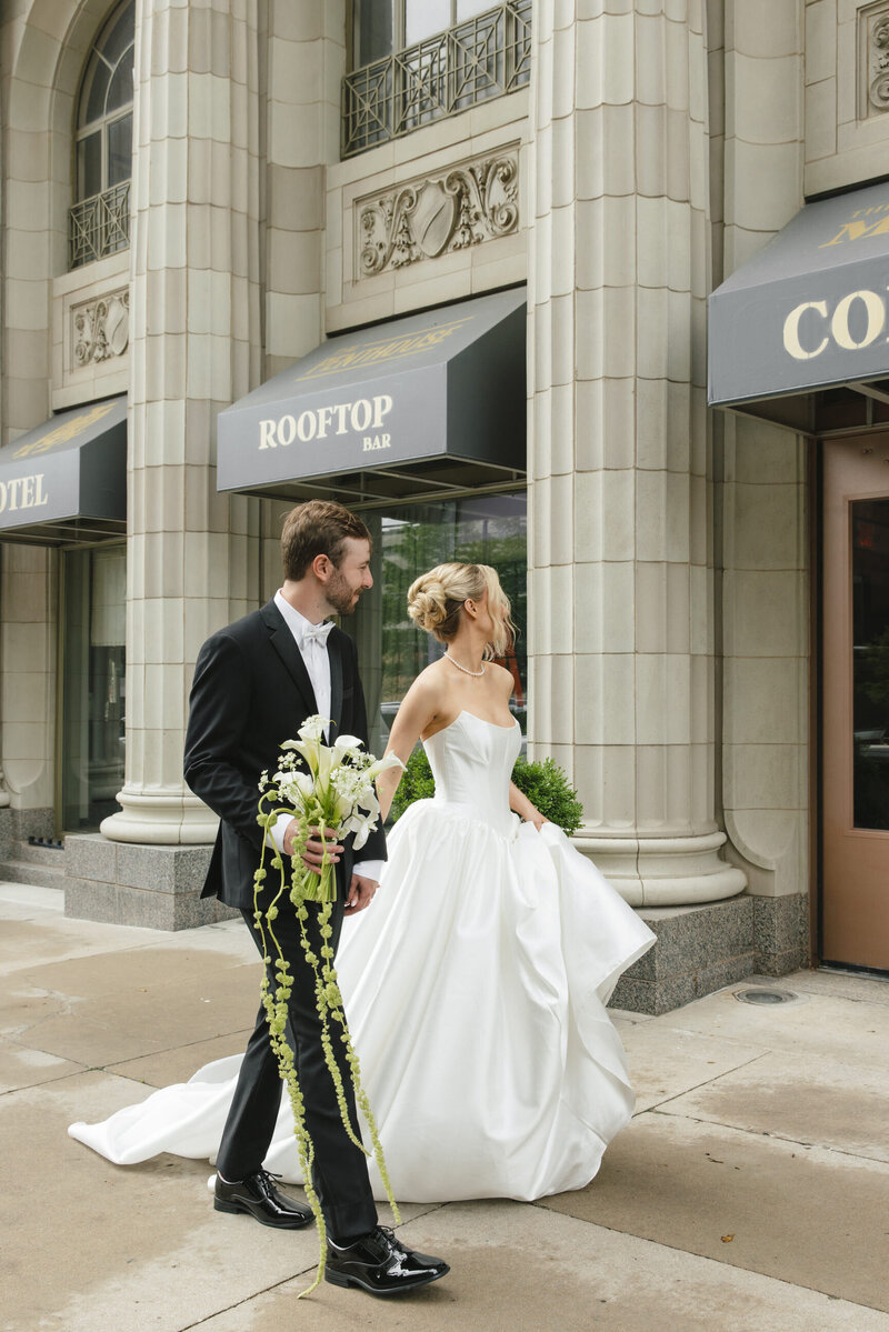 Bride in white dress sitting on marble stairs holding a bouquet of white flowers