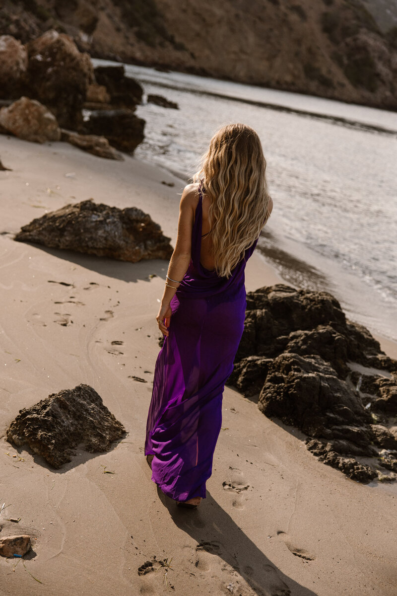 Vrouw in paarse jurk loopt over het strand in Ibiza tijdens shoot.