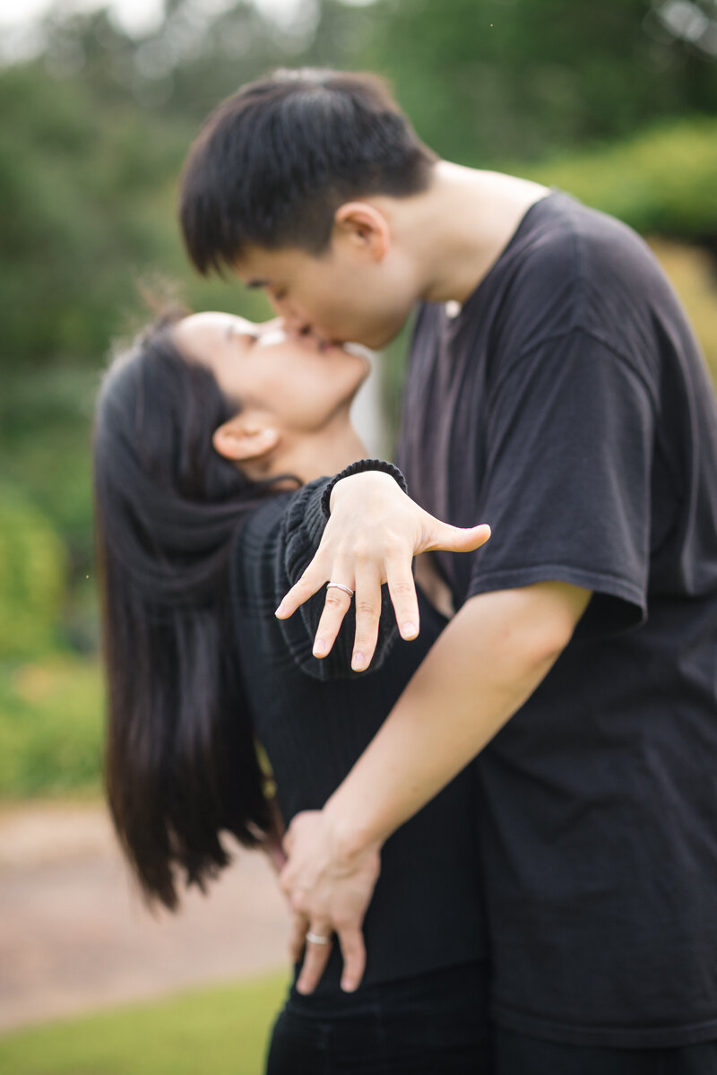 Professional proposal photography in Charlotte NC at Daniel Stowe Conservancy - man and woman kiss as she holds out her hand showing her new engagement ring.