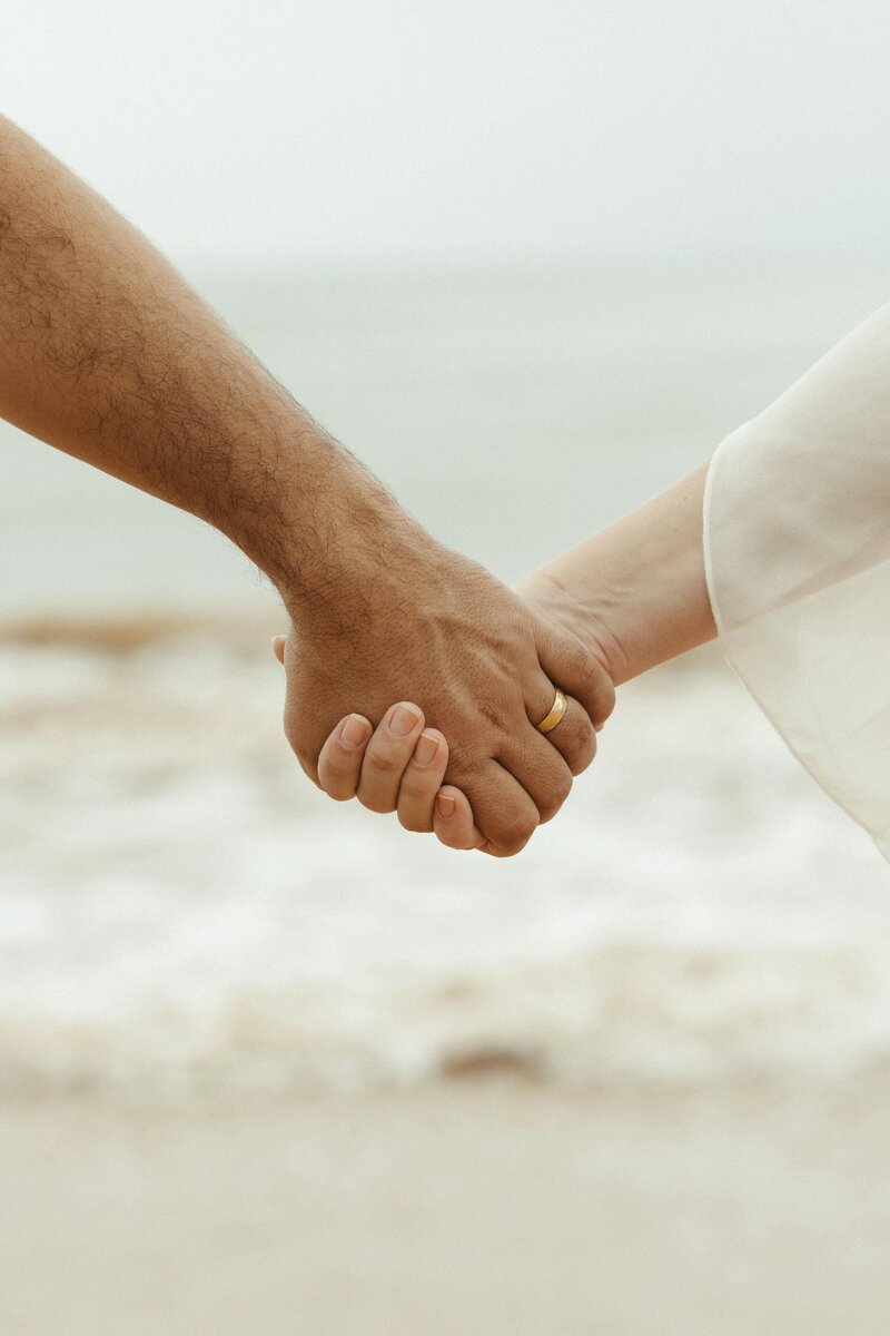 two people holding hands on the beach, showing supportive vibes only