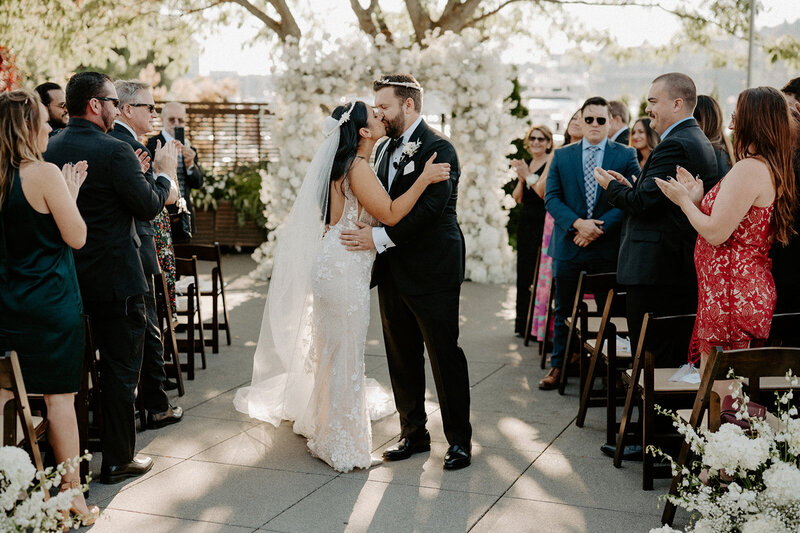 Celebrate the love with this beautiful moment as the bride and groom share a kiss at their outdoor ceremony. Explore more romantic wedding moments.