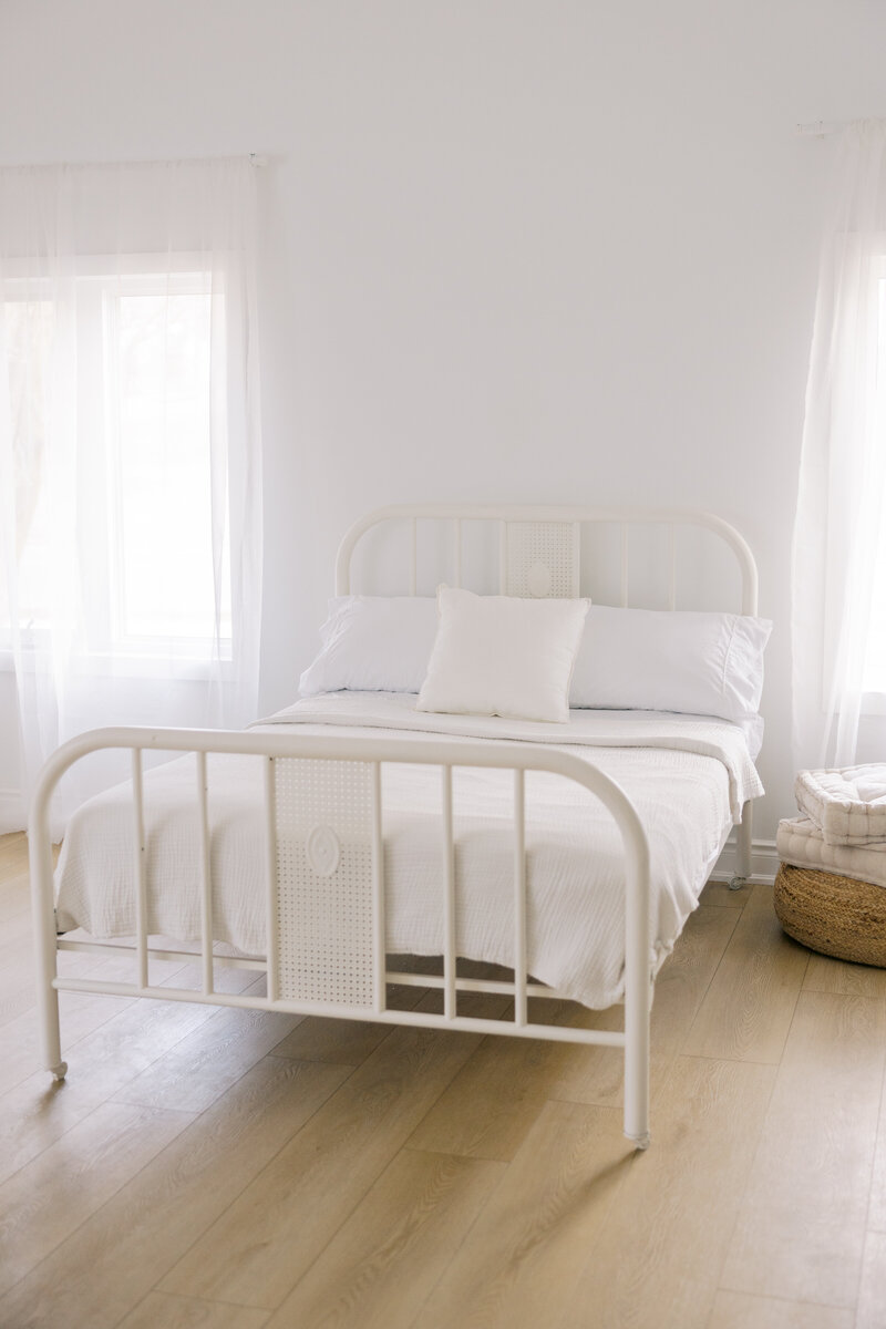 The light bright airy studio with natural wood floors and a white metal bed frame with white bed sheets