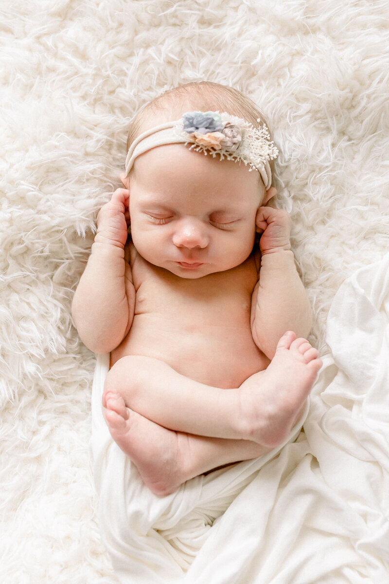 In studio newborn session of baby girl on cream fur blanket and swaddled in cream wrap and flower headband. Brandon, Mississippi Photographer.