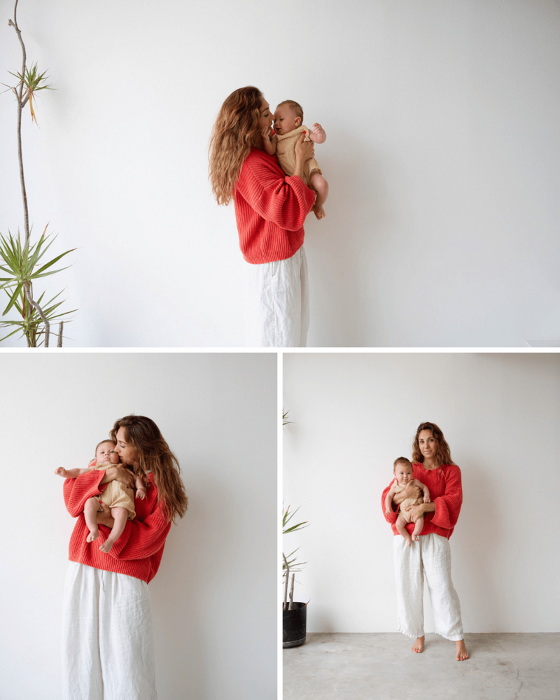 female wearing red sweater and white linen pants holding baby wearing yellow onesie in costa mesa studio