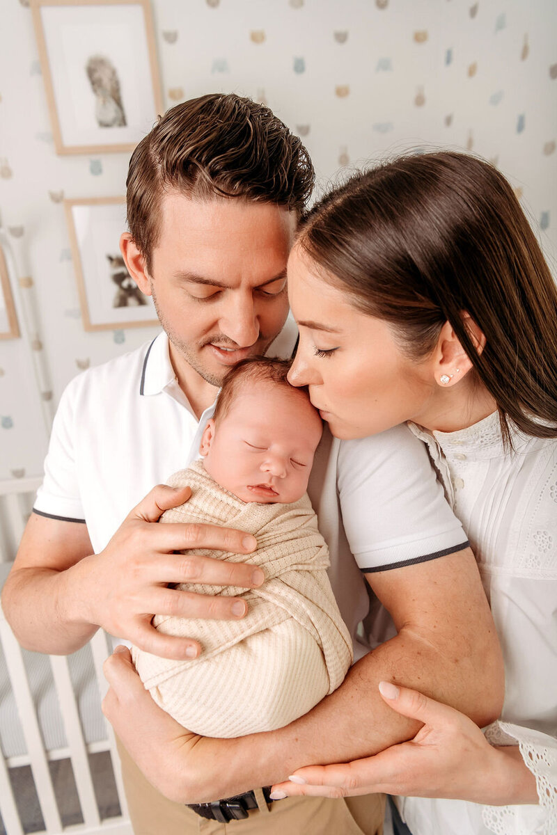Connecticut newborn photographer documents new parents lovingly holding their swaddled baby in bright nursery
