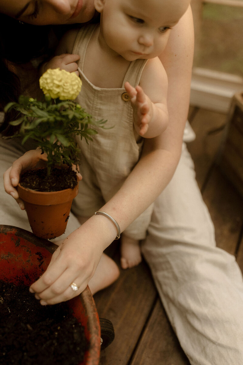 A mother helps her toddler with a potted flower. 