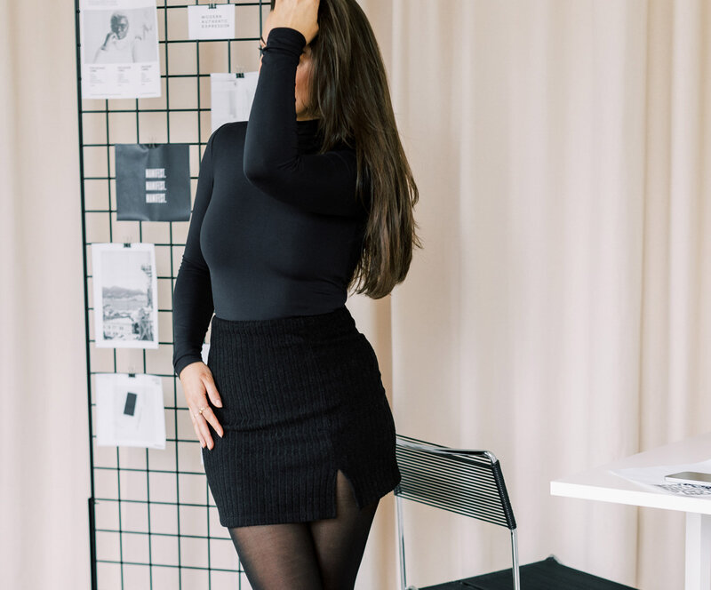 woman holding her hand up to her forhead in black shirt, black skirt and black stockings standing in a website design studio