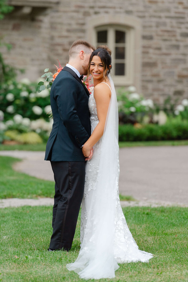 a groom kissing his bride's ear and making her giggle outside Eaton Hall.  Captured by Ottawa wedding photographer JEMMAN Photography