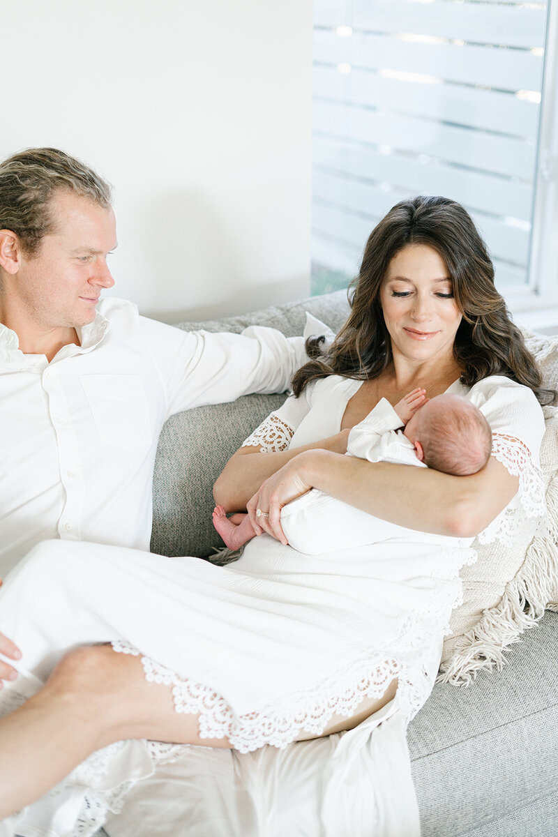 mom and dad snuggling on a couch with newborn baby in arms