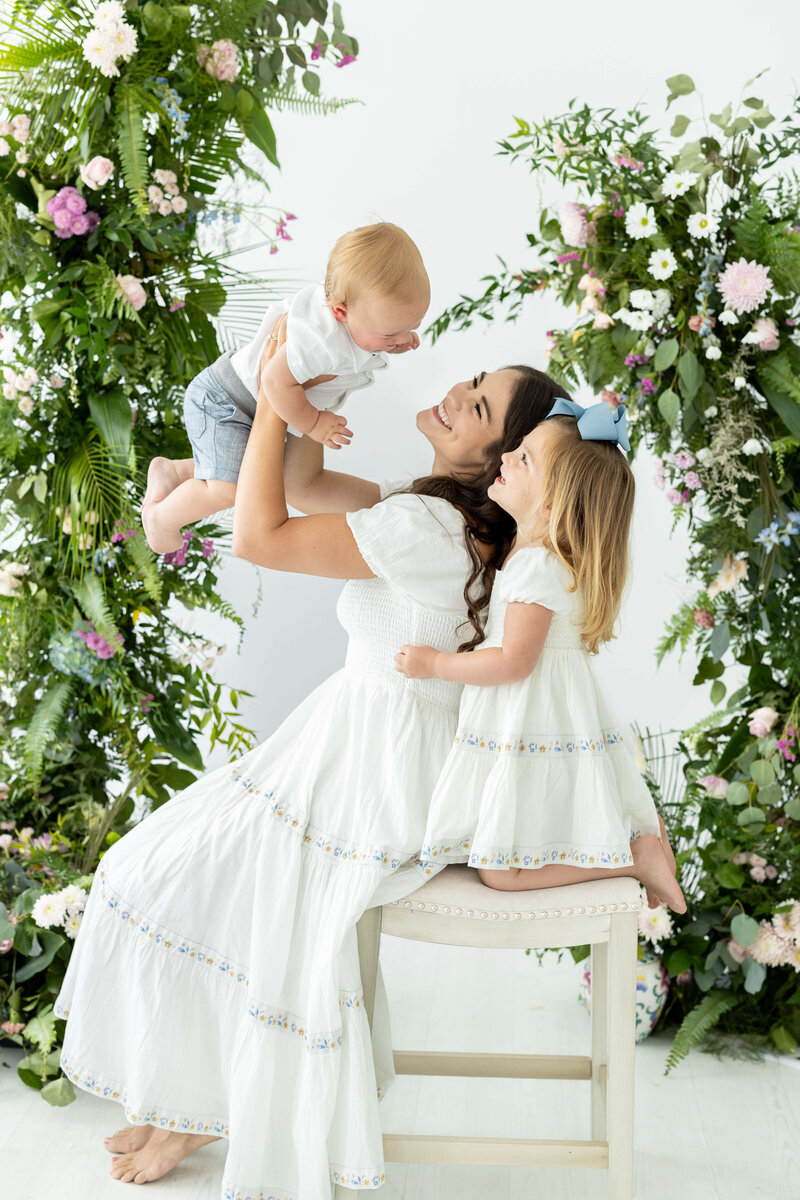 Mom holding son with daughter holding onto mom surrounded by flowers for mini model rep  program