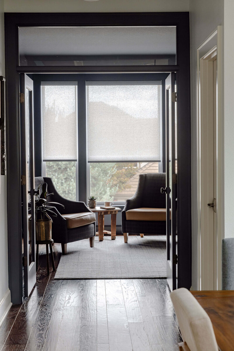 A peek through a doorway into the study featuring two chairs in front of windows and a side table between them.