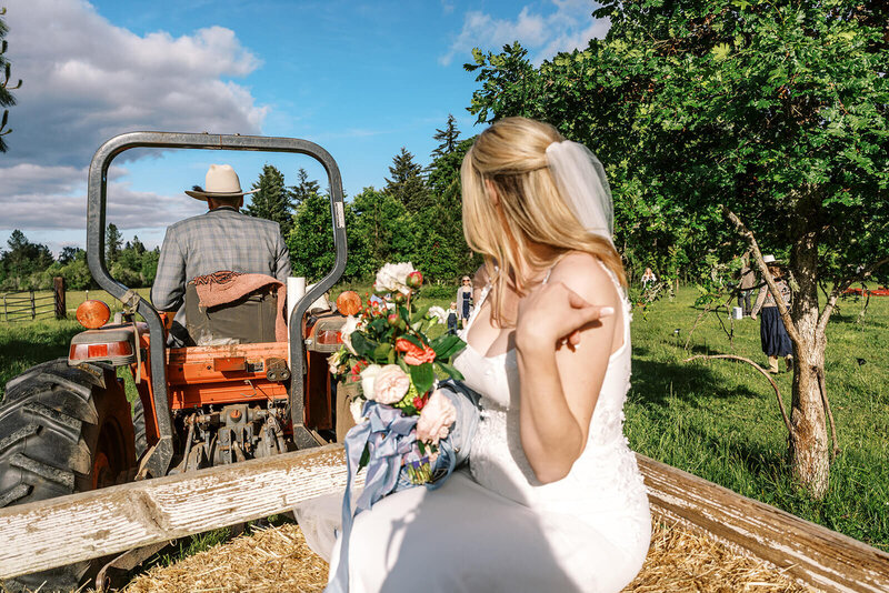 A bride on a hayride pulled by a tractor at her Veneta Farm Wedding.