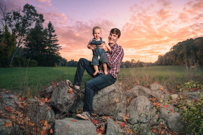boston family photographer corey flint holding baby on stone wall at sunset