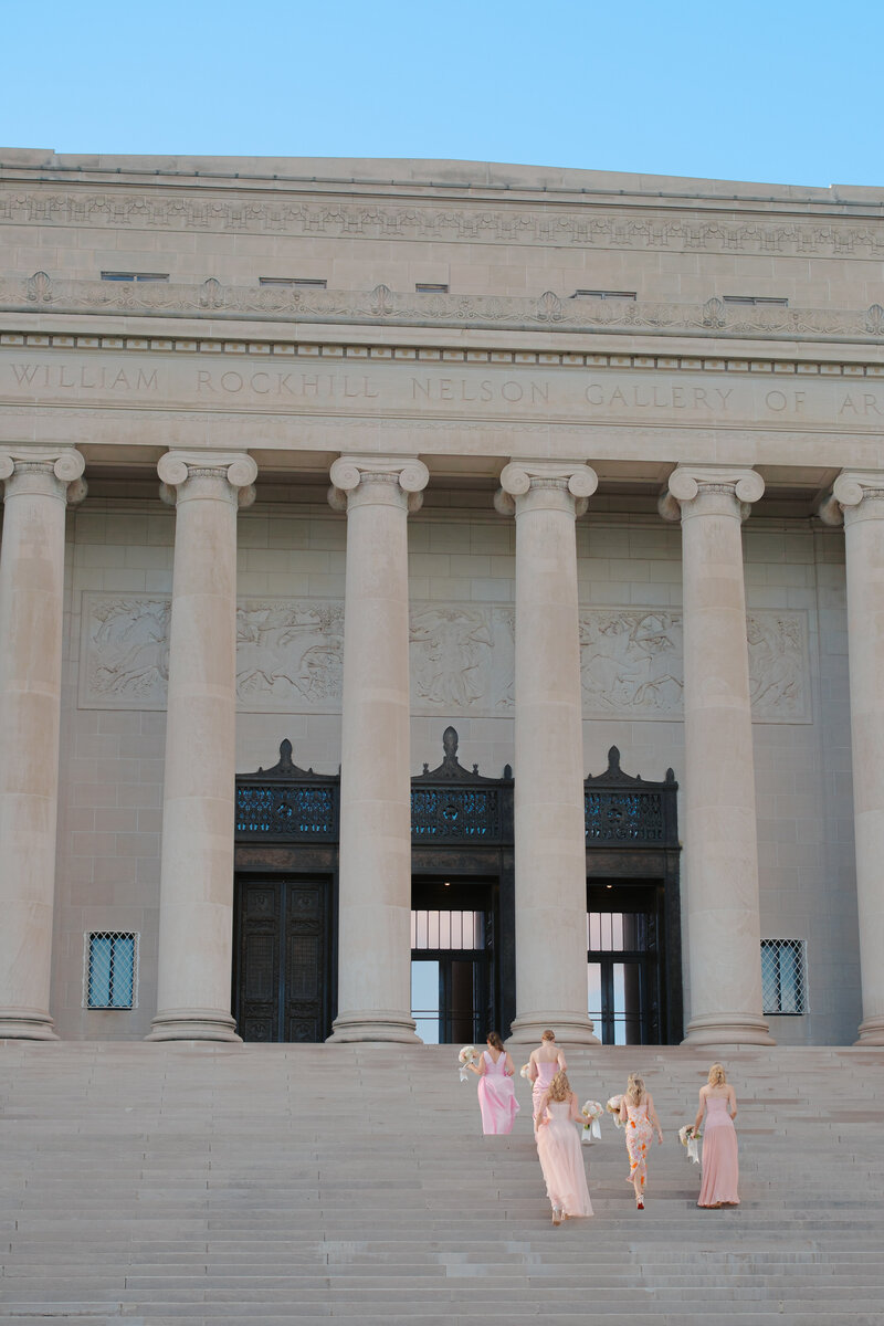 bridesmaids in pink gowns walking up the steps of the Nelson-Atkins Museum in Kansas City, MO