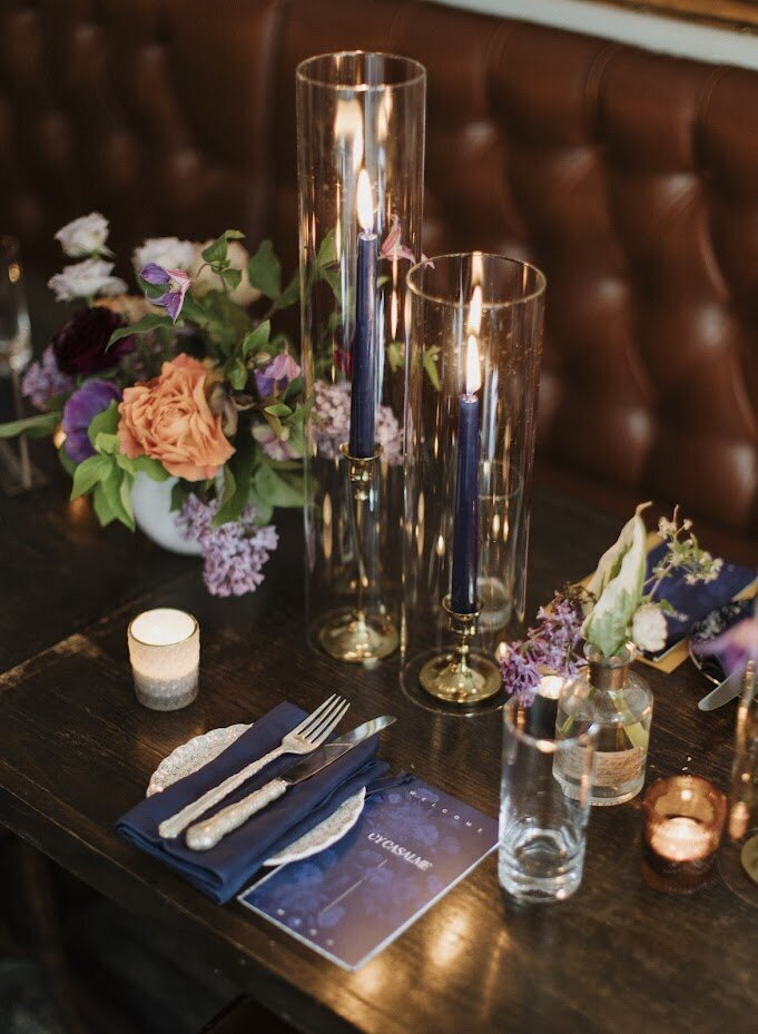 A navy blue dinner menu sits on a table with navy blue tapered candles and mauve flowers at a wedding at North & Navy in Ottawa, designed by Frid Events.
