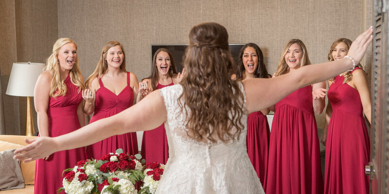 The bride reveals her dress to her bridesmaids on her wedding day.