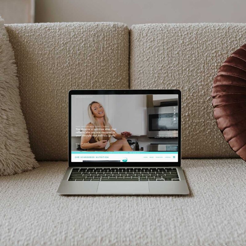 A cozy scene featuring a laptop resting on a couch, surrounded by soft pillows, perfect for Zoe Schroeder Nutrition work.
