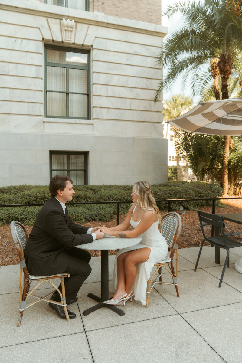 Tattooed couple laughing and holding a parasol in matching pink outfits during a lakeside photoshoot