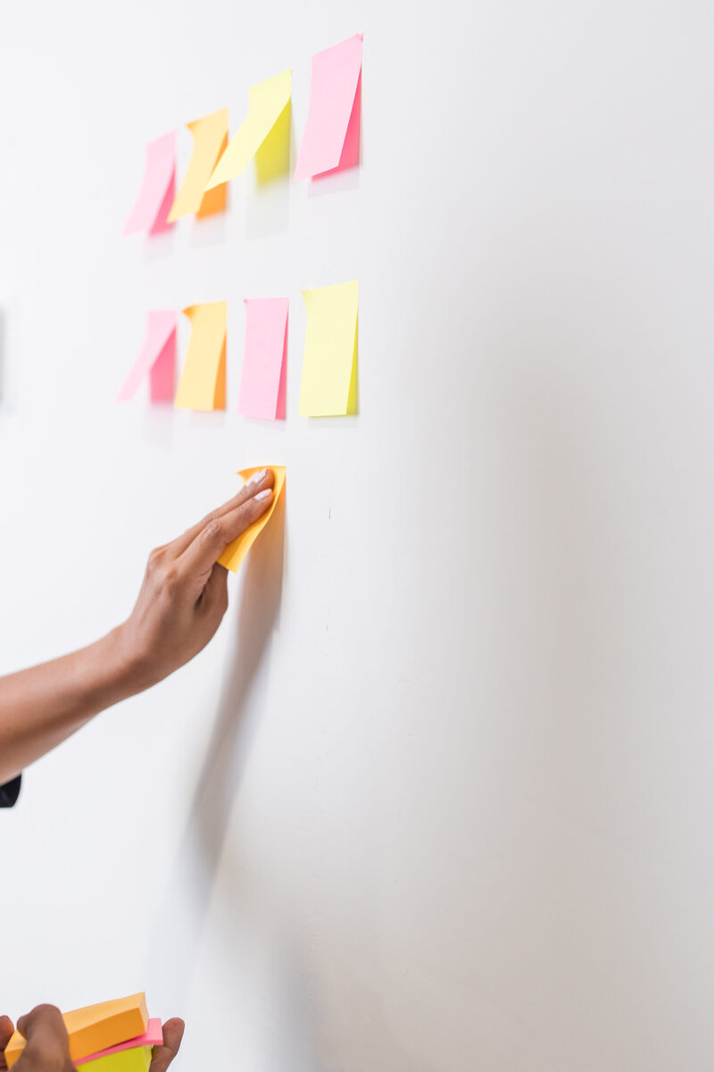 Woman putting pink and yellow post it notes on wall
