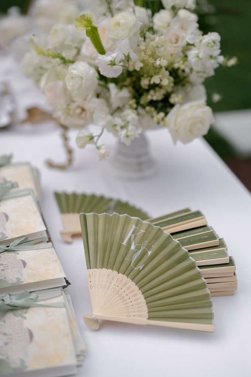 Sage green hand fans and white florals set out for ceremony guests