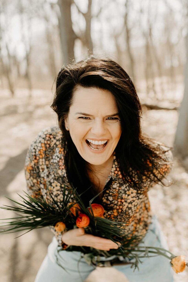 Kathleen Oh laughing and leaning forward with leaves and flowers in her hand