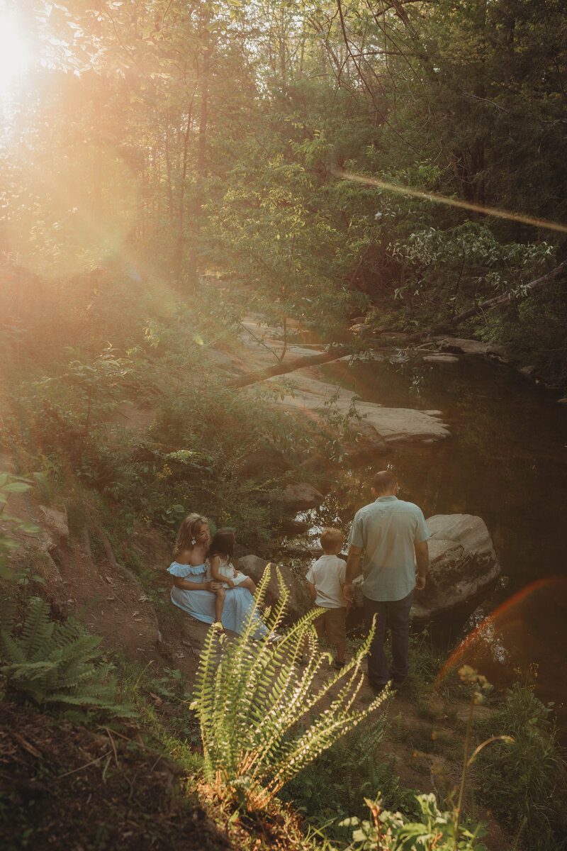 A family sitting and standing by a creek in Blacksburg, Virginia