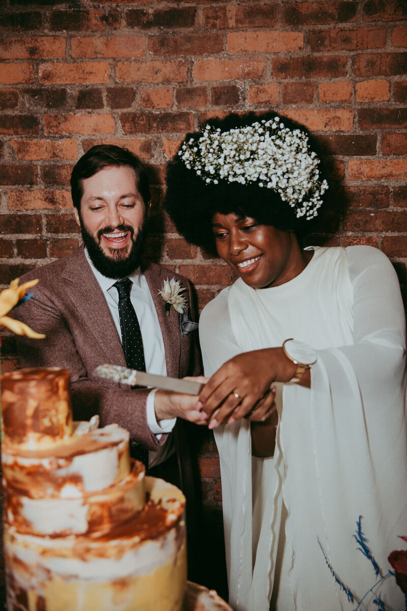 NYC intimate wedding couple cutting nine cakes cake with vintage happy isles salon dress and baby's breath floral hairpiece