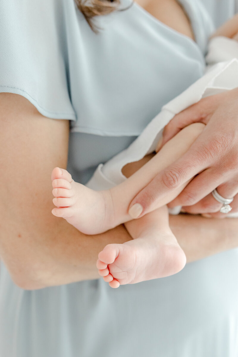 Close up of baby feet as mother in blue dress holding her newborn baby