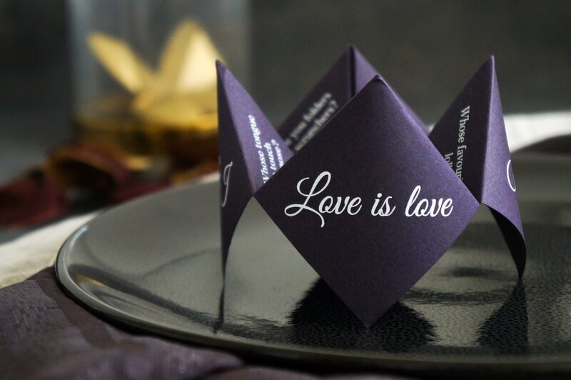 Purple fortune-teller card with "Love is love" printed on the side at a wedding reception table