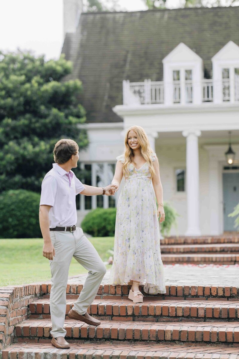 man helping his fiance down the front steps of a home