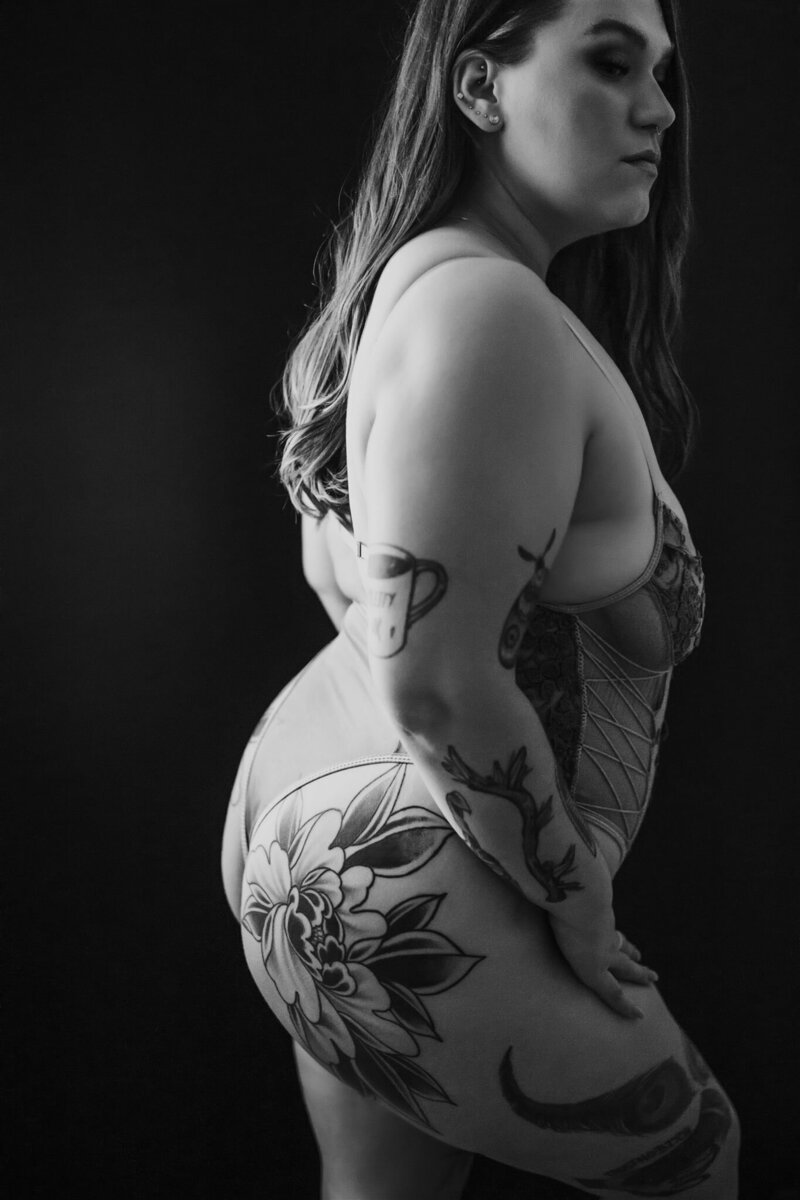 curvy tattooed boudoir model posing against black background
