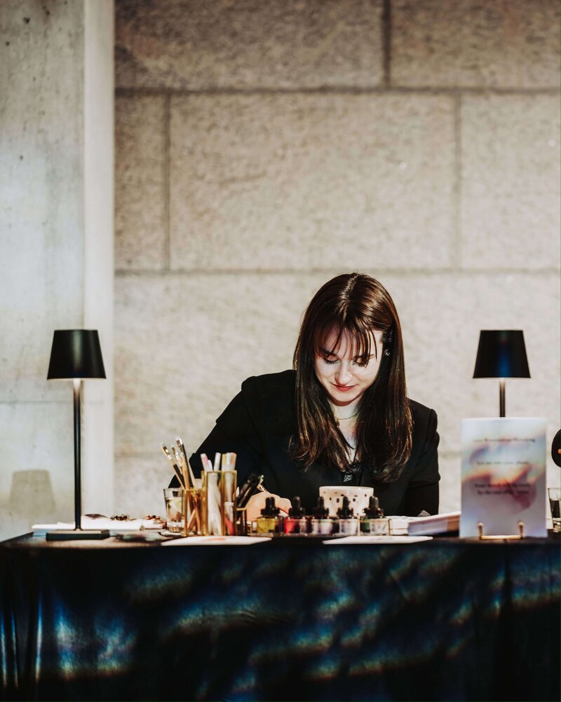 Stephanie Anne Illustration, a Montreal-based live wedding sketch artist, working at her desk with watercolor supplies and art materials