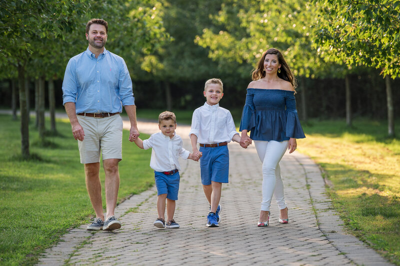 A family of 4 with coordinated outfits holding hands and walking down a path at a park.