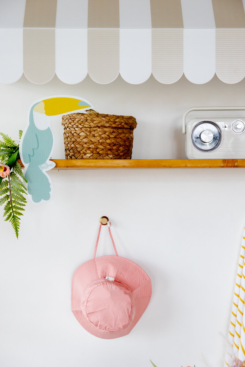 Shelf on party wall decorated with hook and hat, toucan, basket and radio.