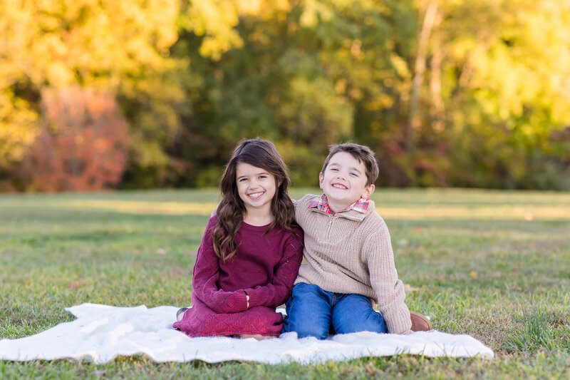 A brother and sister sitting in a field in Northern VA and snuggled up together on a blanket.