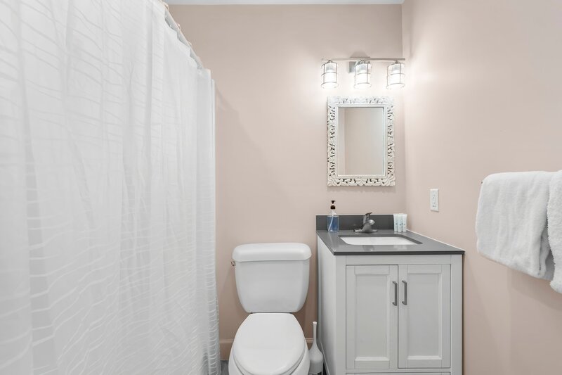 Bright guest bathroom with modern vanity, framed mirror, and full shower with white curtain, perfect for family convenience.
