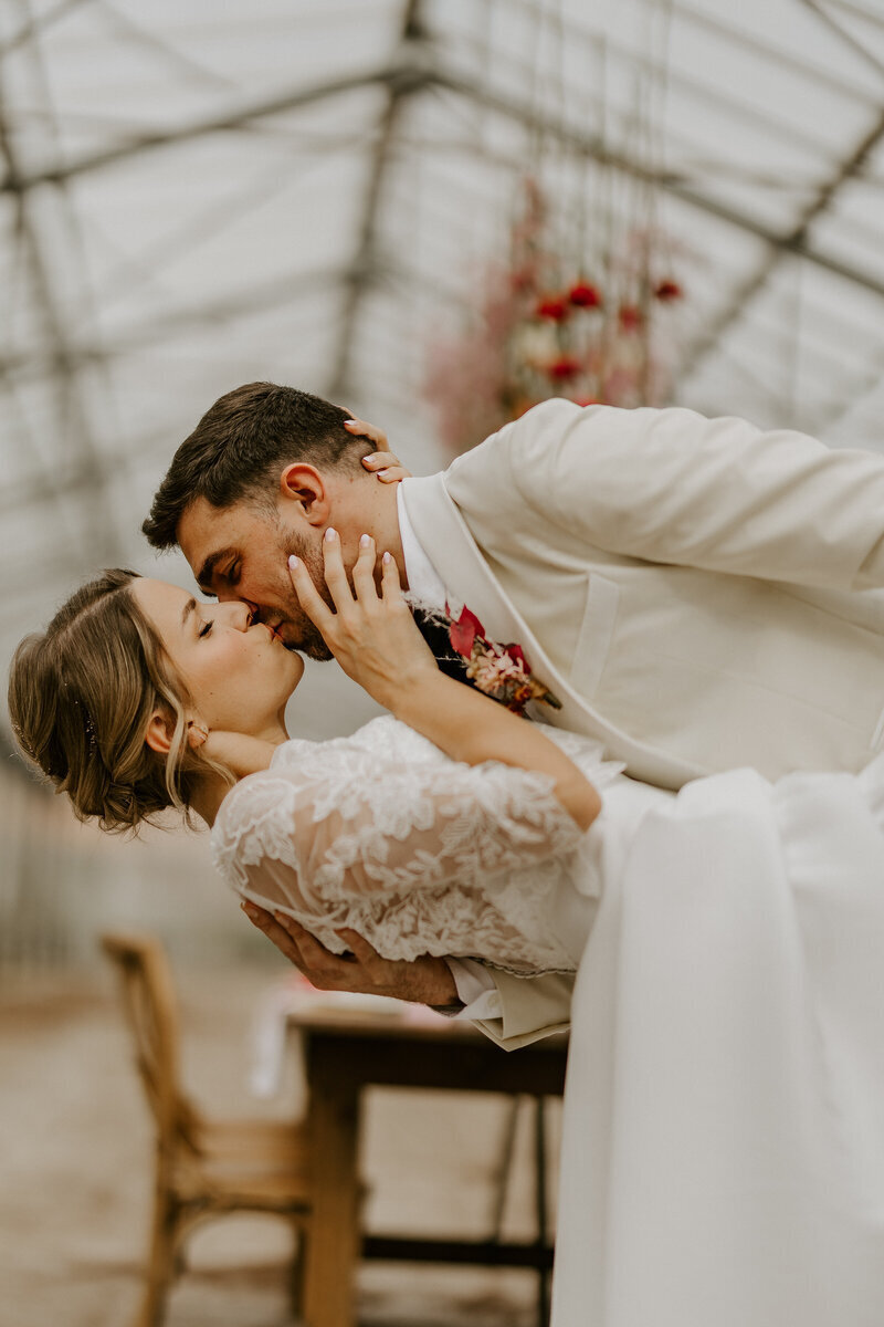 Le mari bascule la mariée en arrière pour un baiser dans un décor de mariage sous verrière industrielle. PhOtographie réalisée lors du workshop photographie de amriage organisé par Laura.