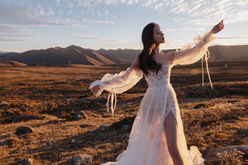 A bride photographed in the golden evening light in a wild field with. mountains in the background.