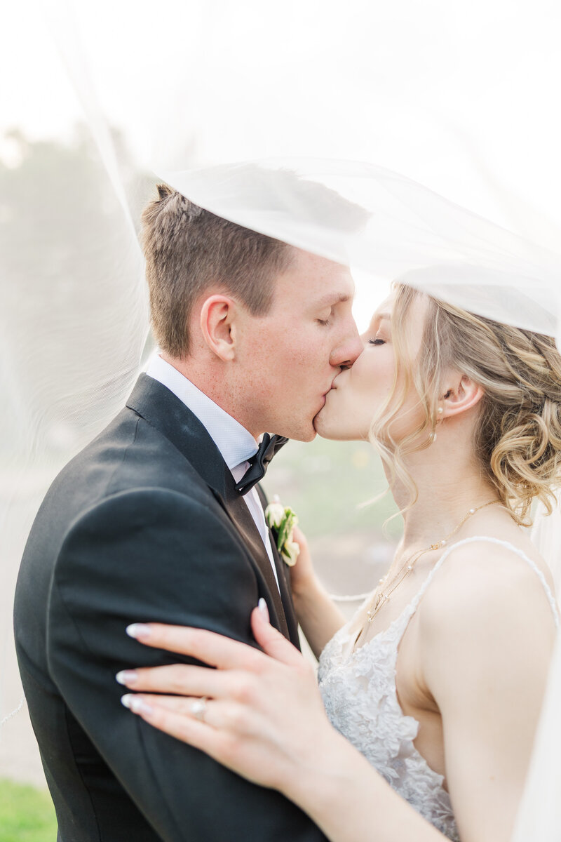bride and groom kissing while underneath her veil