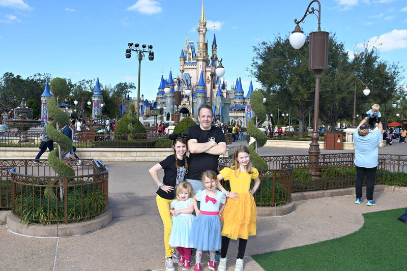 Dad in a Princess security t-shirt with four girls in Disney Princess inspired outfits in front of Cinderella's Castle at Magic Kingdom