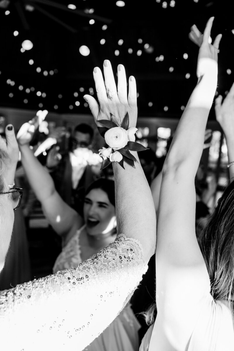 black and white of wedding guests with their hands raised dancing on the dance floor