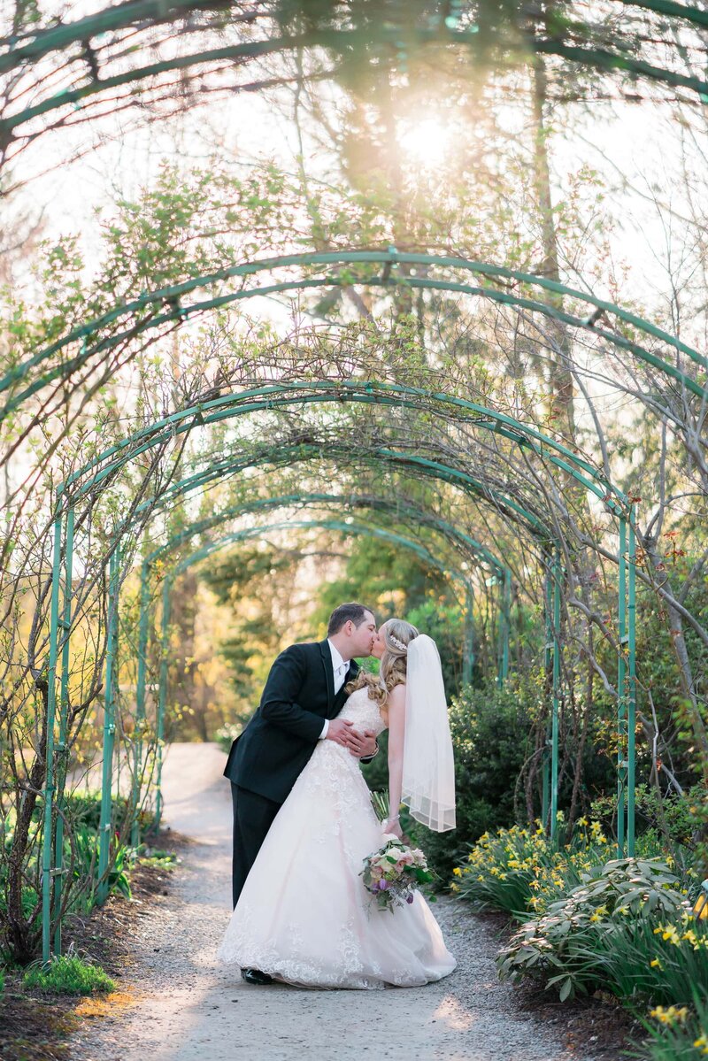 Bride and groom kiss under arbor