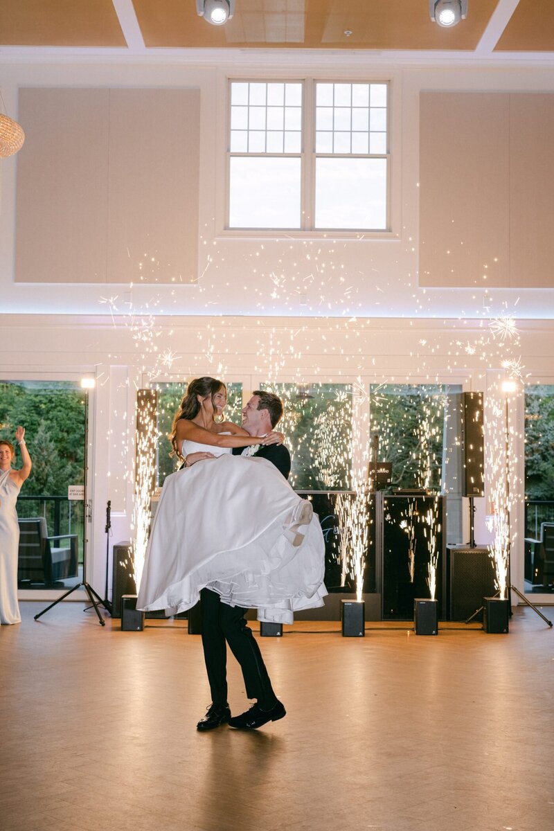 George lifting Anya during their first dance as sparklers rise behind them