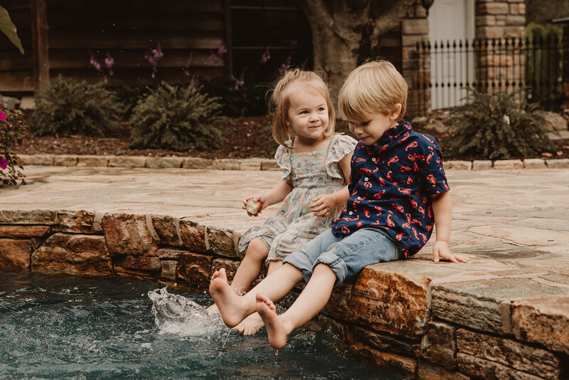 Two small kids sitting at the edge of a pool kicking their feet in the water 