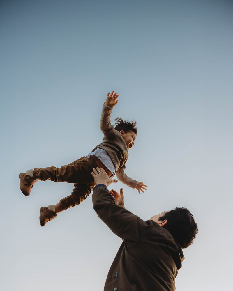 son laughing while being thrown in the air during a sunset family session in The Woodlands, Texas