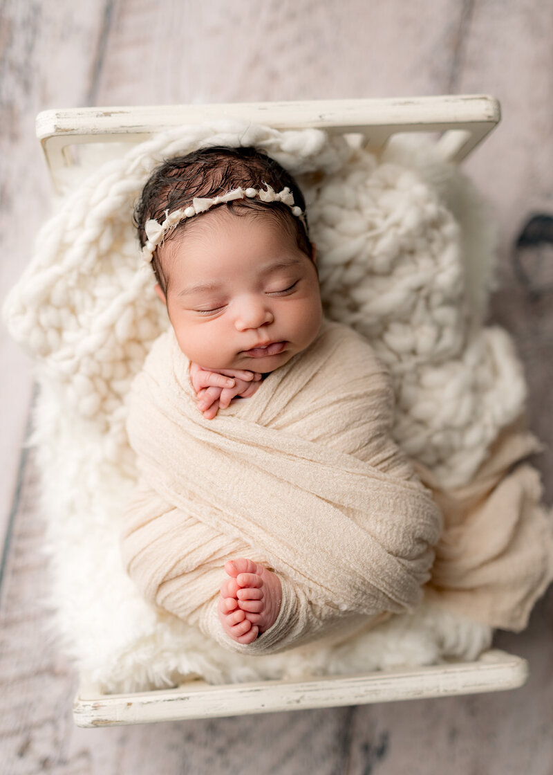 baby girl lying in a little white bed wearing a cream bow headband