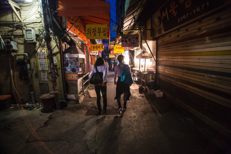 View from behind of two people walking through a Seoul market at night