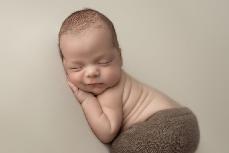 Newborn boy with a slight smirk in cozy brown tones – timeless side pose portrait in Paris, Ontario.