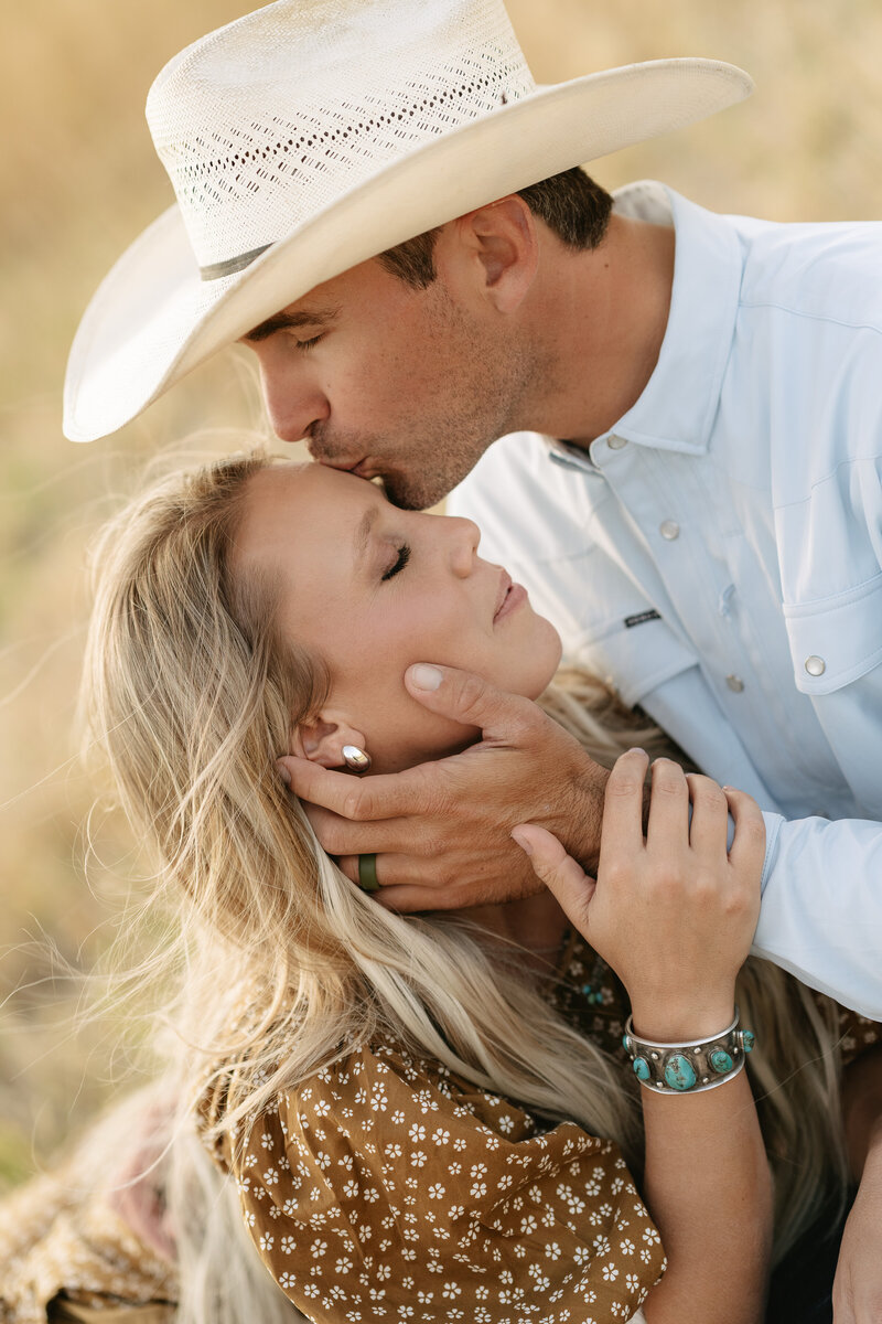 Cowboy kissing his partner’s forehead during an intimate western engagement session