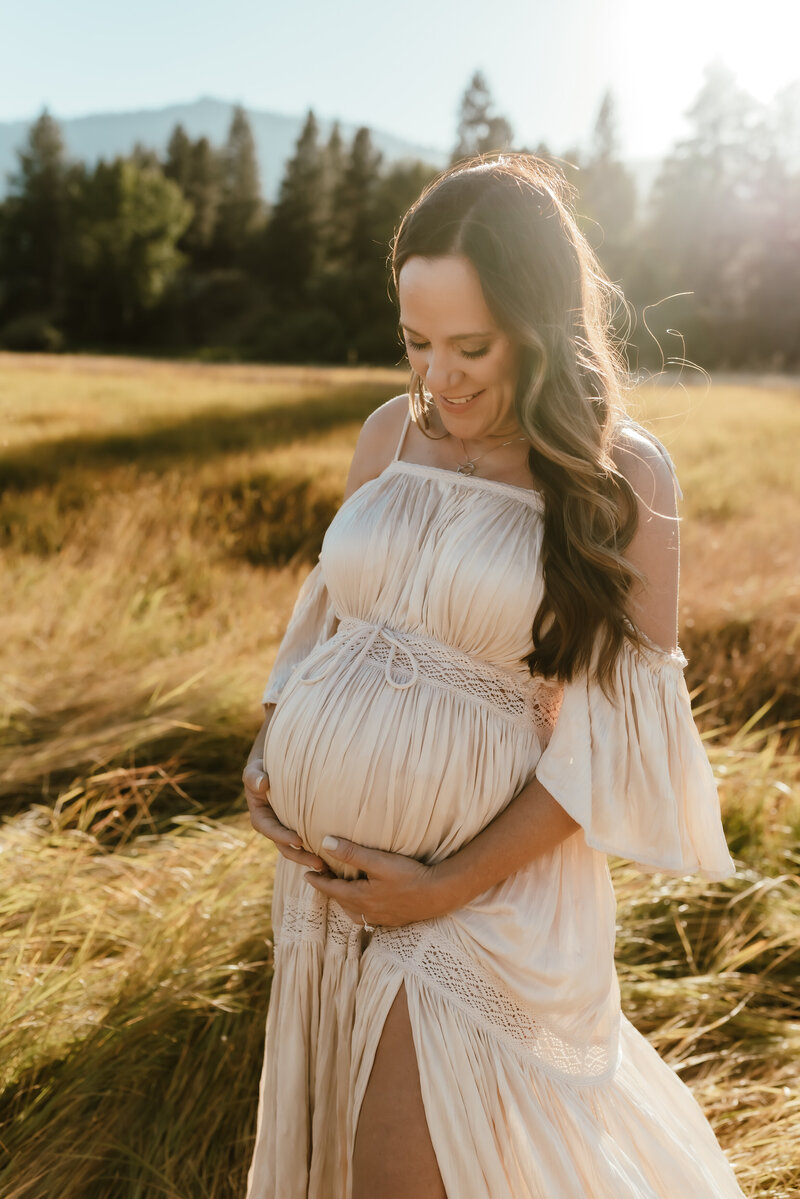 Pregnant mother holding her baby bump in a Tahoe meadow at sunset.